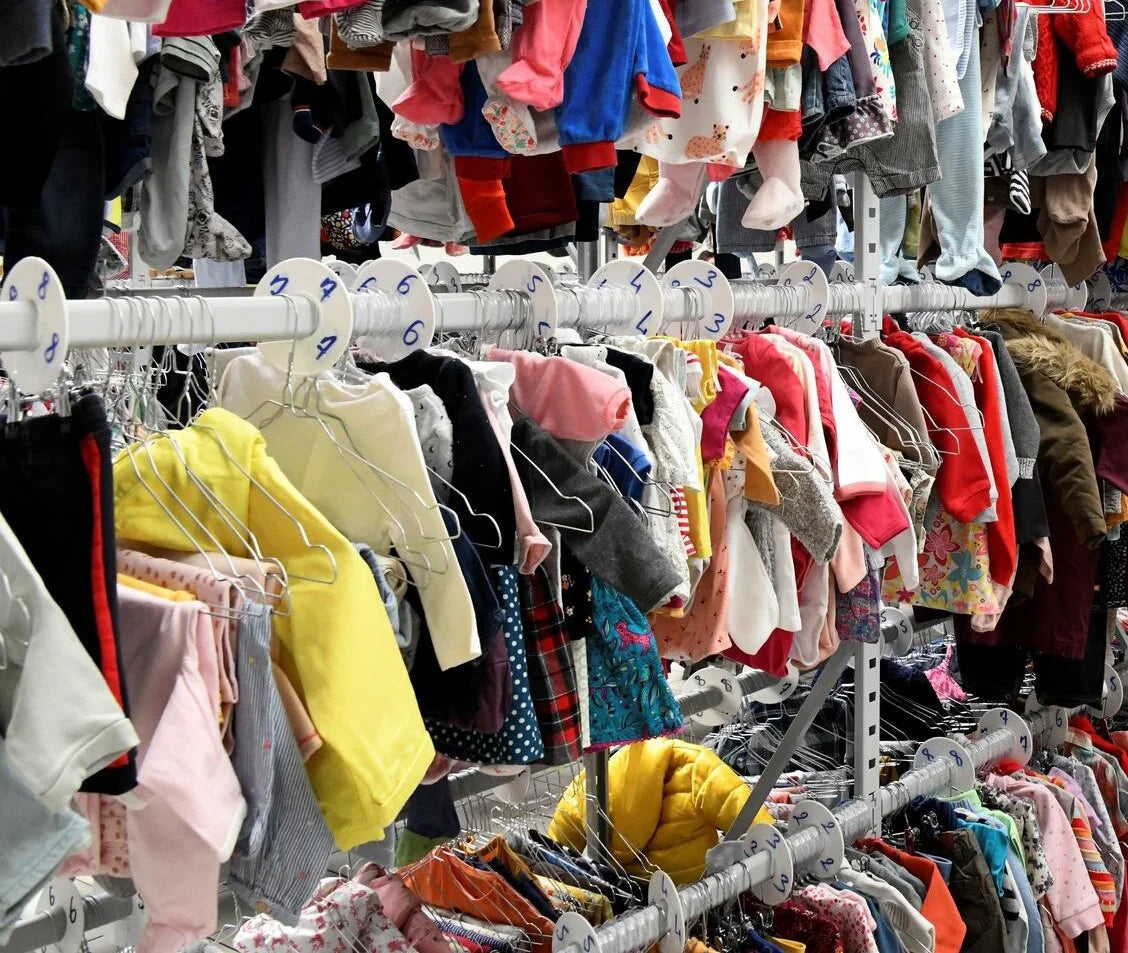 Petits vêtements rangés sur plusieurs portants et cintres dans un espace de vente.